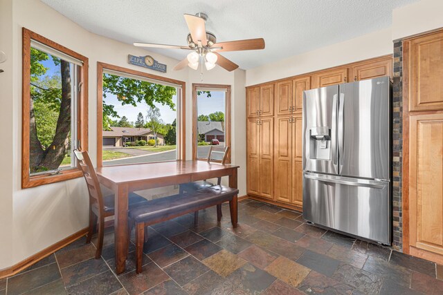 dining area featuring a ceiling fan, baseboards, stone tile flooring, and a textured ceiling