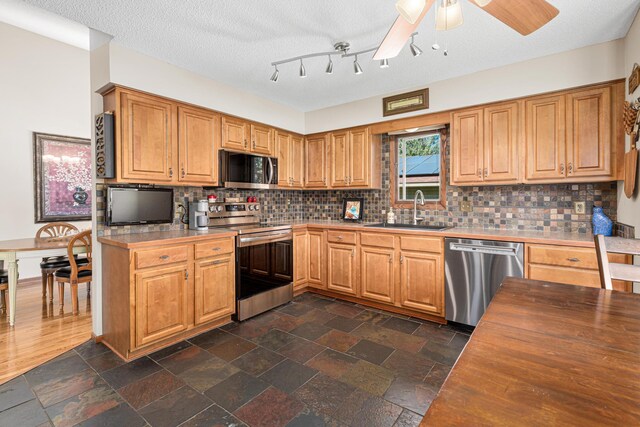 kitchen with appliances with stainless steel finishes, a sink, ceiling fan, wooden counters, and backsplash