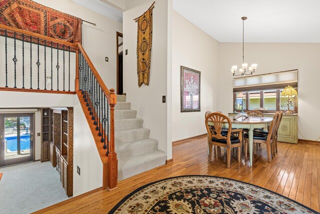 dining area with light wood-style floors, a chandelier, plenty of natural light, baseboards, and high vaulted ceiling