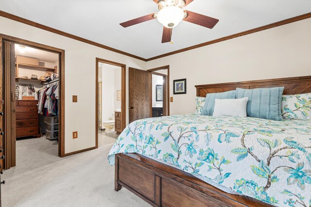bedroom with a walk in closet, light colored carpet, a closet, baseboards, and crown molding