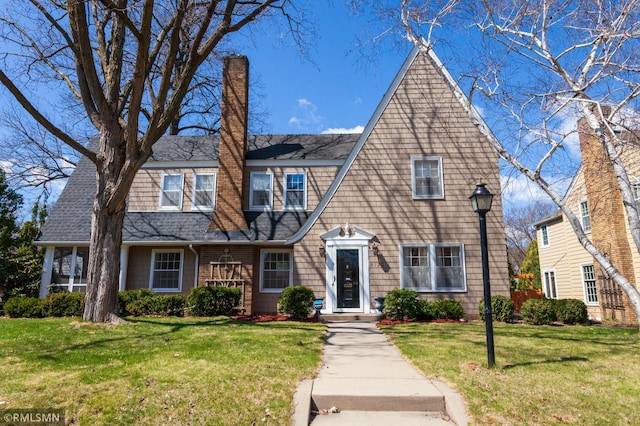 view of front of home featuring a chimney, a front lawn, and roof with shingles