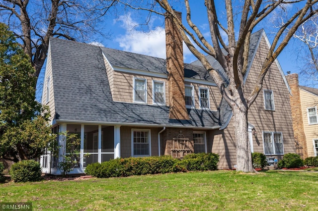 view of front of home featuring a chimney, a sunroom, roof with shingles, and a front yard