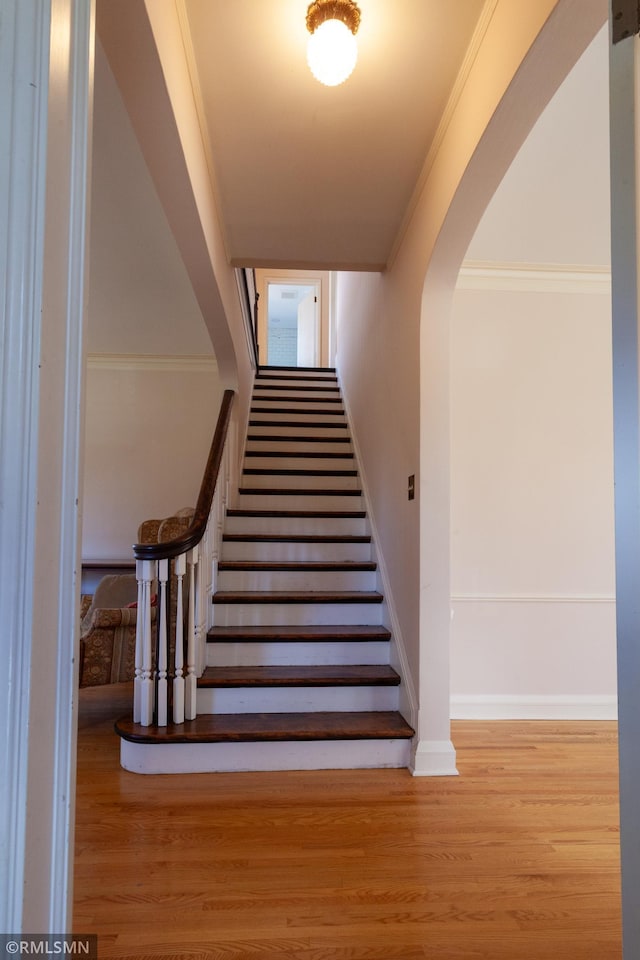 stairway with wood finished floors, arched walkways, baseboards, and crown molding