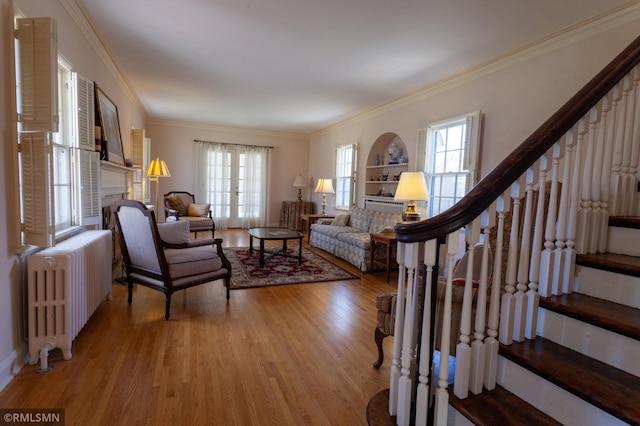 living area featuring radiator heating unit, stairway, light wood finished floors, crown molding, and a fireplace