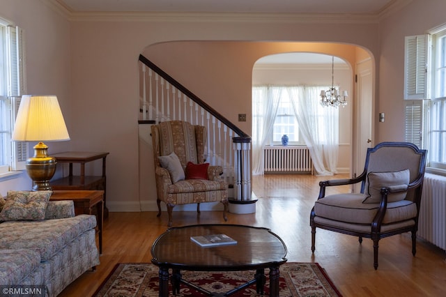 living area with radiator heating unit, arched walkways, wood finished floors, healthy amount of natural light, and ornamental molding