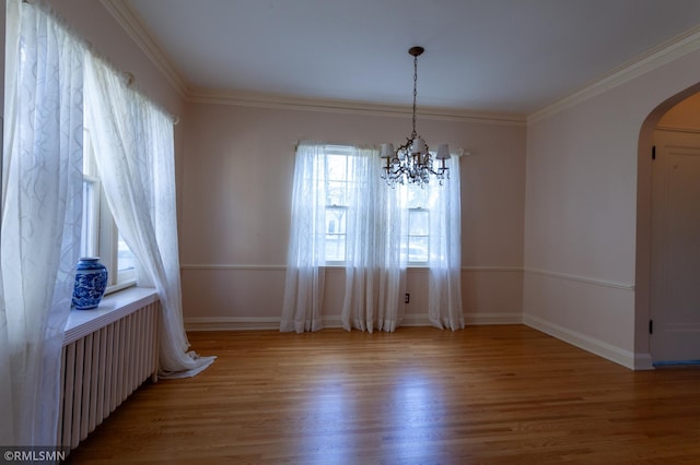 unfurnished room featuring arched walkways, wood finished floors, ornamental molding, radiator, and a chandelier