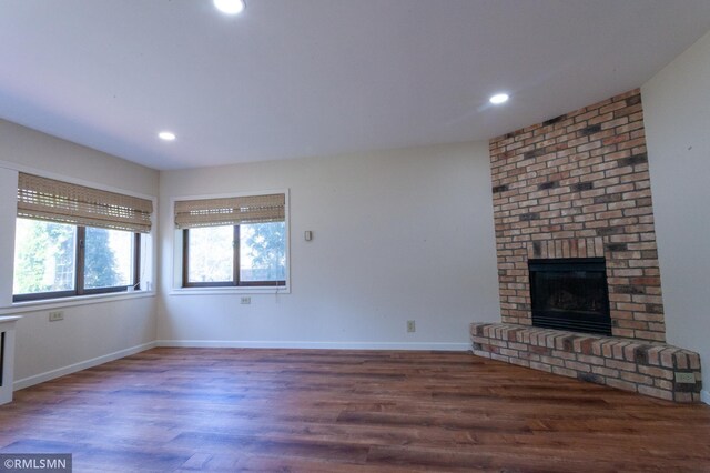 unfurnished living room with a brick fireplace, wood finished floors, baseboards, and recessed lighting