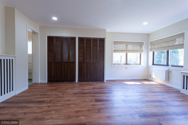 unfurnished bedroom featuring two closets, wood finished floors, recessed lighting, and baseboards