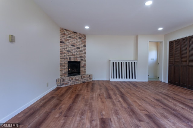 unfurnished living room with wood finished floors, a brick fireplace, baseboards, recessed lighting, and radiator
