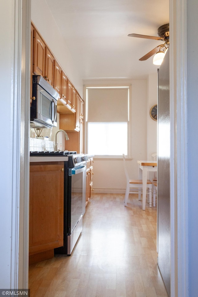 kitchen with stainless steel microwave, a ceiling fan, range with electric cooktop, dark countertops, and light wood-style floors