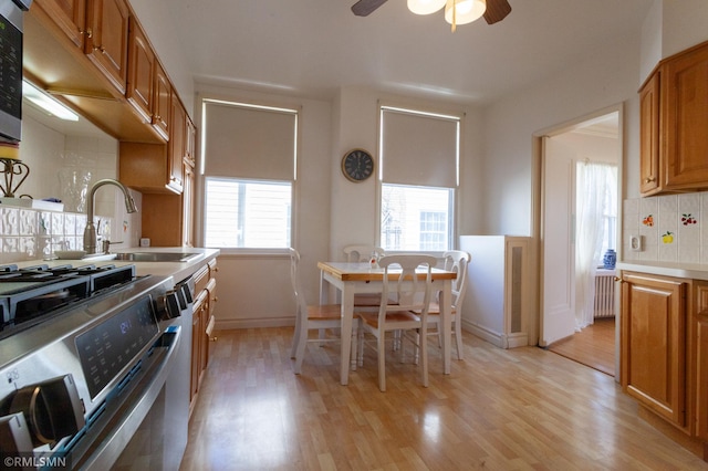 kitchen with stainless steel appliances, radiator heating unit, light wood-type flooring, a sink, and backsplash