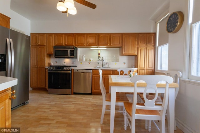 kitchen featuring appliances with stainless steel finishes, a sink, light countertops, backsplash, and brown cabinetry