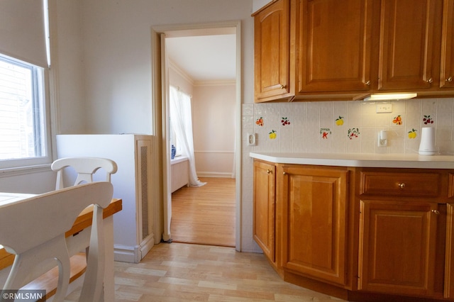 kitchen with light wood-style flooring, light countertops, brown cabinets, backsplash, and crown molding