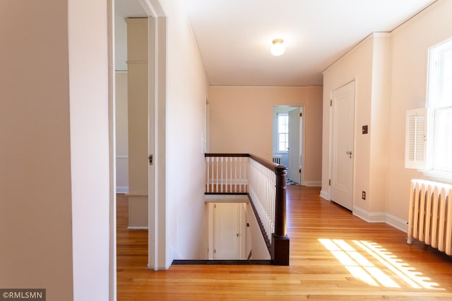 hallway with radiator, light wood-style flooring, an upstairs landing, and baseboards