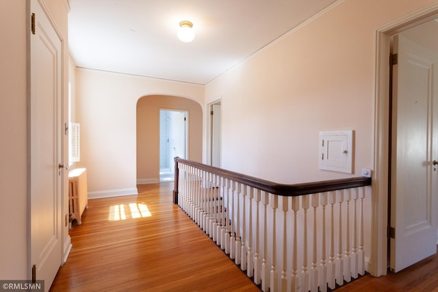 hall with arched walkways, radiator, light wood finished floors, an upstairs landing, and baseboards