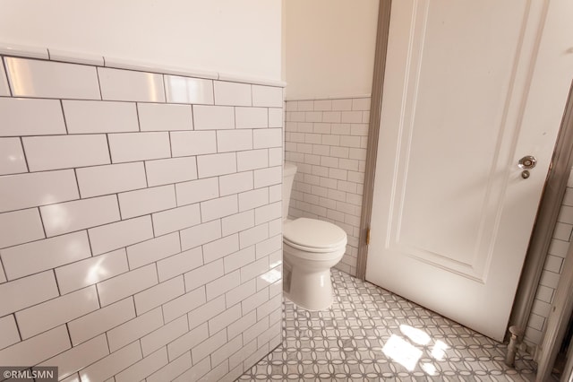 bathroom featuring tile walls, toilet, and a wainscoted wall