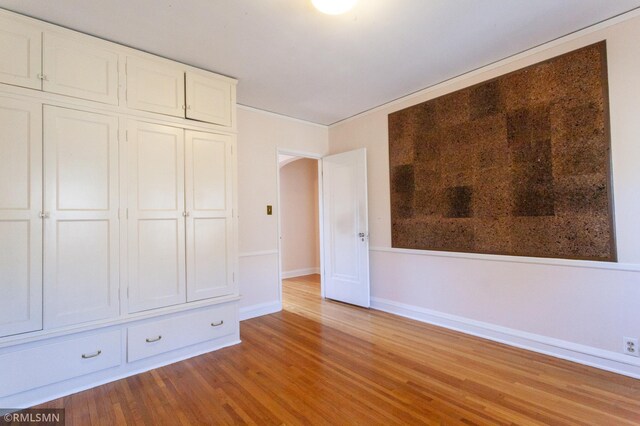 unfurnished bedroom featuring wood finished floors, baseboards, and arched walkways