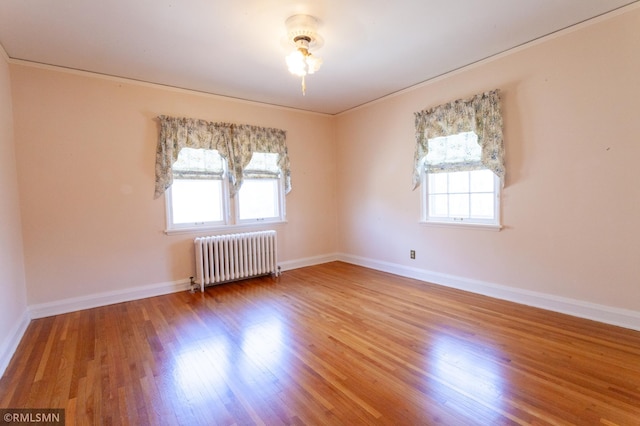 spare room featuring radiator, wood finished floors, baseboards, and ornamental molding