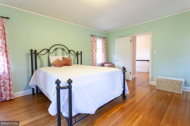 bedroom with wood finished floors, baseboards, and ornamental molding