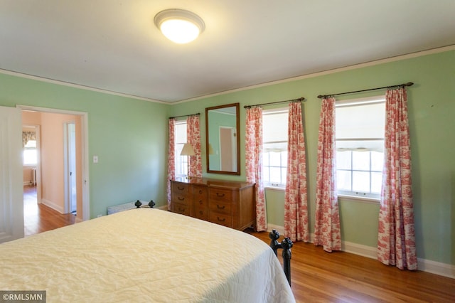 bedroom featuring wood finished floors, multiple windows, crown molding, and baseboards