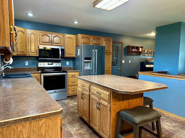 kitchen featuring a breakfast bar area, a kitchen island, a textured ceiling, a sink, and stainless steel appliances