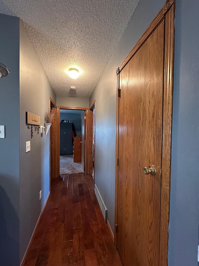 hall featuring baseboards, dark wood-style floors, a textured ceiling, and visible vents