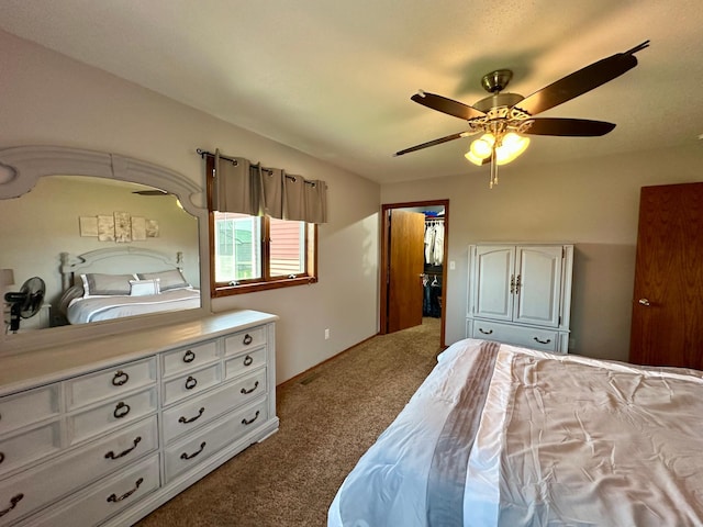 bedroom with a walk in closet, carpet, and a ceiling fan