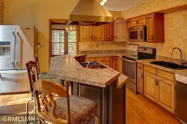 kitchen featuring appliances with stainless steel finishes, a sink, light wood-type flooring, island range hood, and a kitchen bar