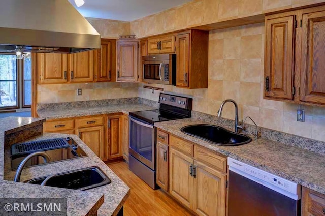 kitchen with wall chimney range hood, appliances with stainless steel finishes, decorative backsplash, and a sink