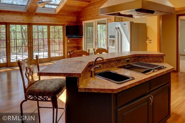 kitchen featuring high end fridge, a sink, vaulted ceiling with skylight, extractor fan, and french doors
