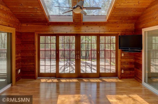 interior space featuring wood walls, lofted ceiling with skylight, wood finished floors, and ceiling fan