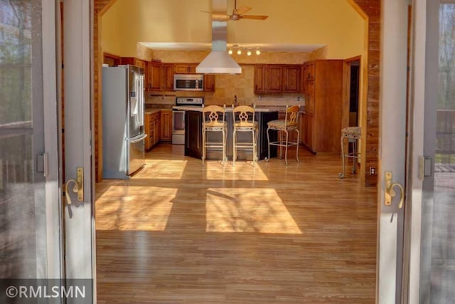kitchen featuring a breakfast bar area, light wood-type flooring, brown cabinets, a ceiling fan, and stainless steel appliances