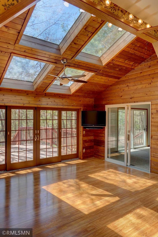 unfurnished living room featuring french doors, lofted ceiling with skylight, wood finished floors, and wooden walls