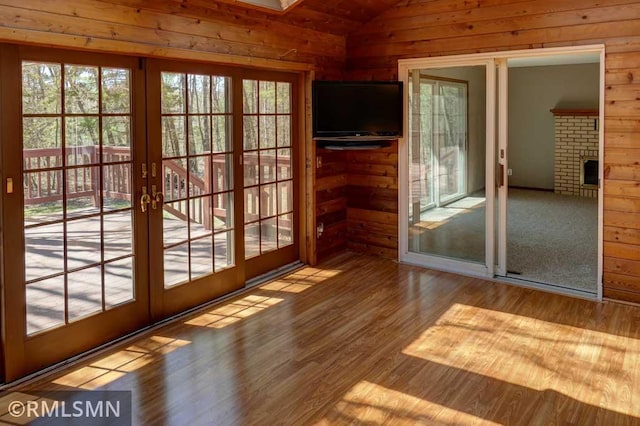 entryway featuring french doors, a brick fireplace, wood walls, wood finished floors, and lofted ceiling