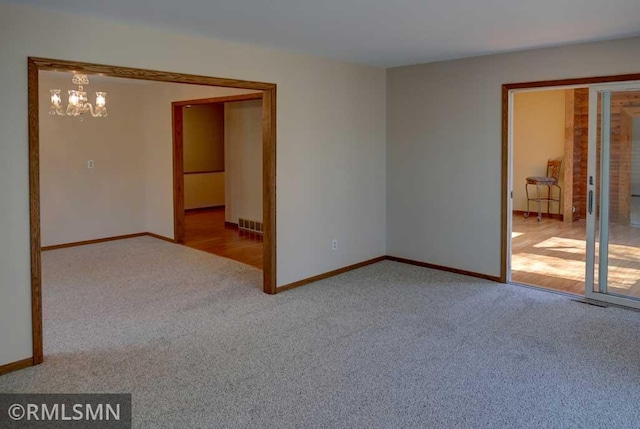 carpeted spare room with an inviting chandelier, baseboards, and visible vents