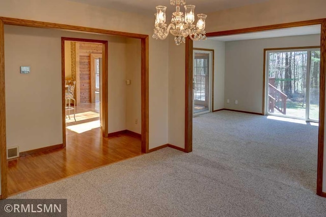 carpeted empty room with baseboards, a chandelier, and visible vents