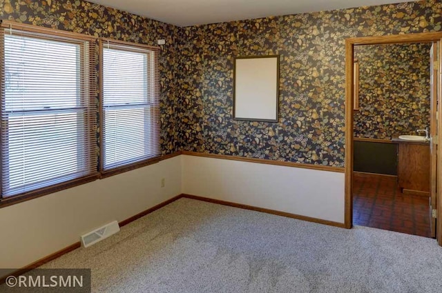 carpeted empty room with a sink, baseboards, wallpapered walls, and visible vents
