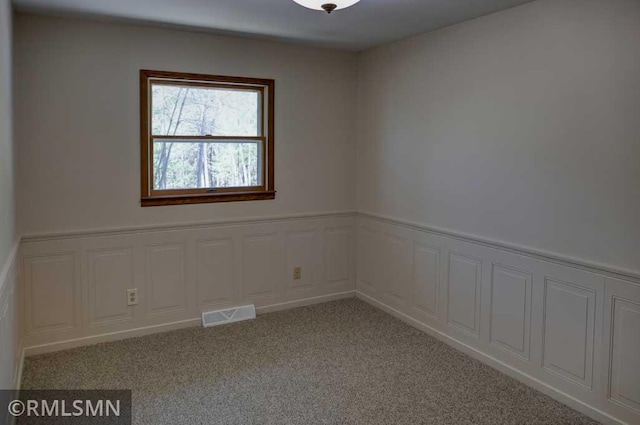 empty room featuring a wainscoted wall, carpet, and visible vents