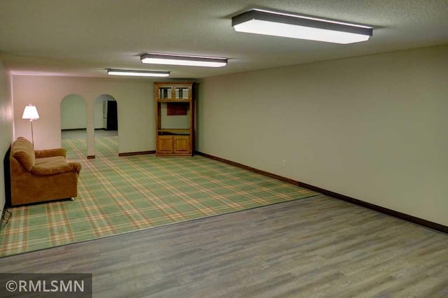 below grade area featuring baseboards, arched walkways, and wood finished floors