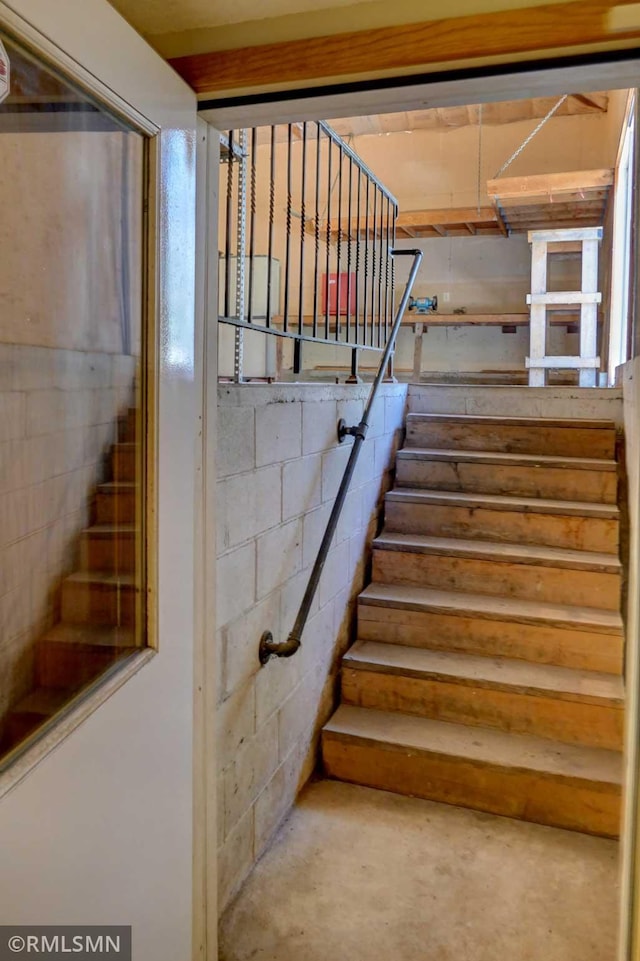 staircase featuring concrete block wall and concrete floors