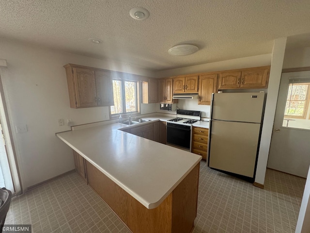 kitchen with a peninsula, white appliances, light countertops, under cabinet range hood, and a sink