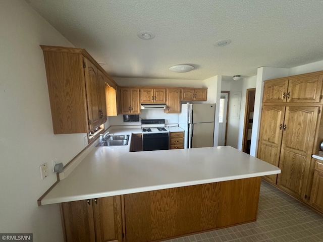 kitchen with exhaust hood, a sink, gas range gas stove, freestanding refrigerator, and a peninsula