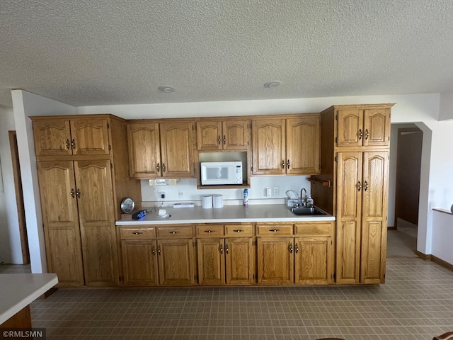 kitchen featuring brown cabinets, light countertops, a sink, and white microwave