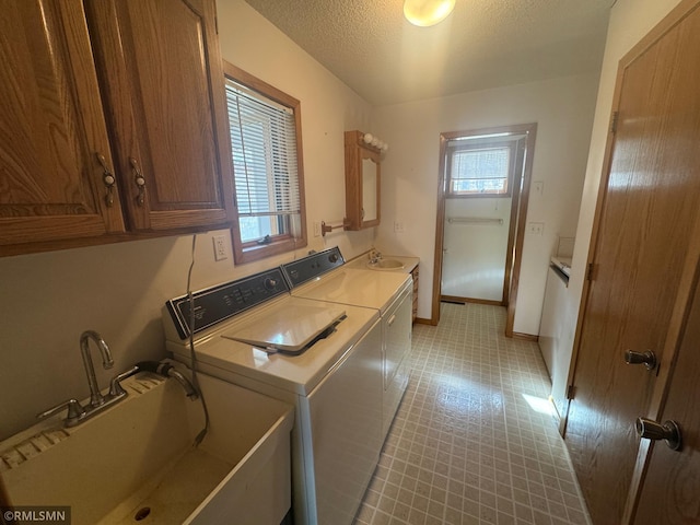 clothes washing area featuring washing machine and clothes dryer, cabinet space, a sink, a textured ceiling, and baseboards