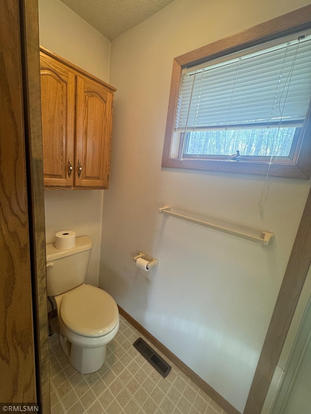bathroom with visible vents, toilet, baseboards, a textured ceiling, and tile patterned floors