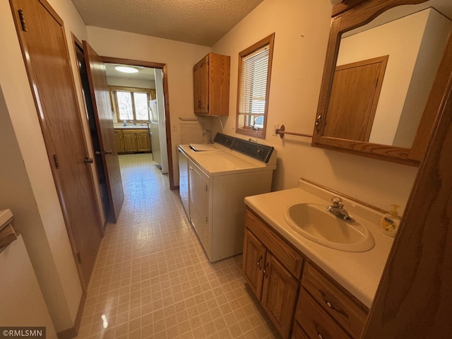 laundry area with a textured ceiling, washing machine and dryer, a sink, and light floors
