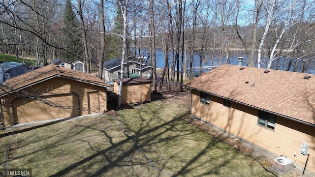 view of side of property featuring roof with shingles, an outbuilding, a shed, a yard, and a water view