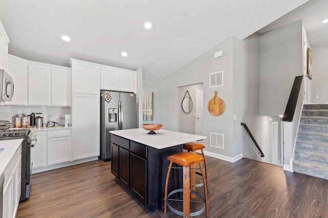 kitchen with stainless steel appliances, lofted ceiling, a breakfast bar, dark wood finished floors, and white cabinetry