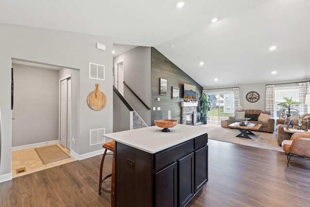 kitchen featuring a kitchen breakfast bar, light countertops, dark wood-style floors, vaulted ceiling, and a stone fireplace