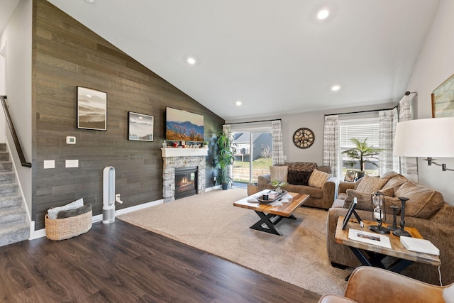 living area featuring wood finished floors, a stone fireplace, recessed lighting, stairway, and high vaulted ceiling